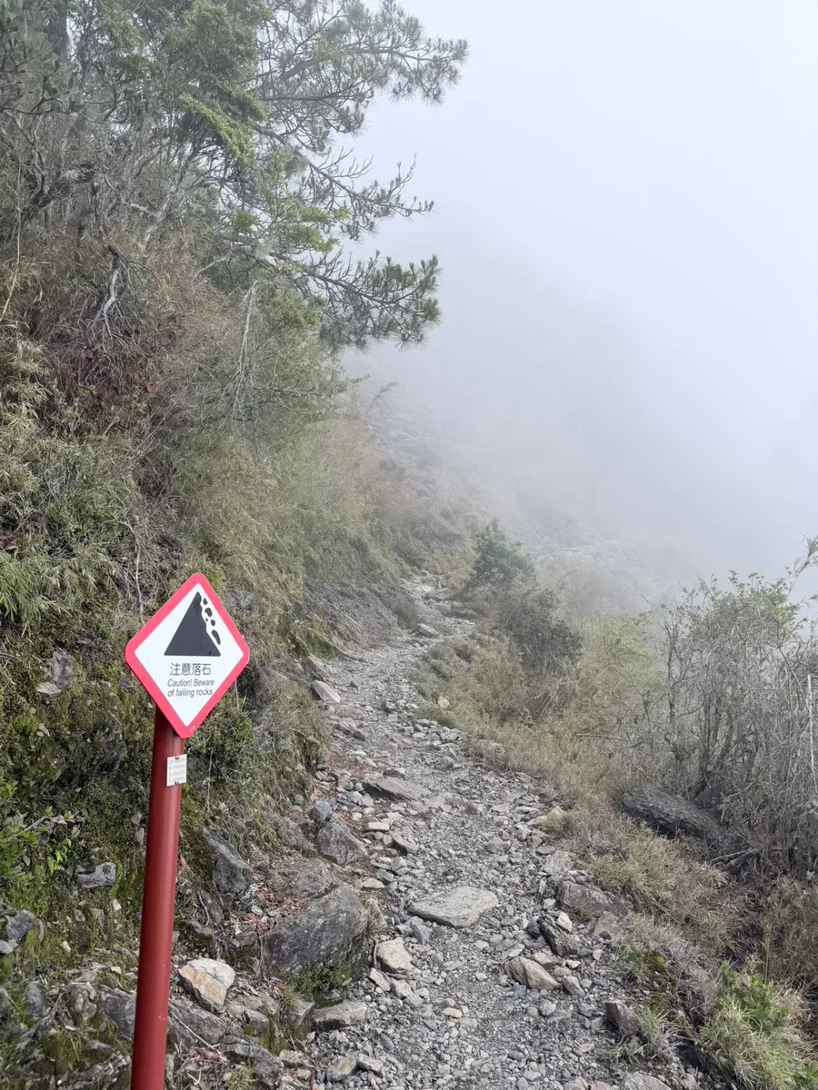 玉山步道旁的「注意落石 Caution! Beware of falling rocks」警告標誌,後方是滿地碎石的橫切路段