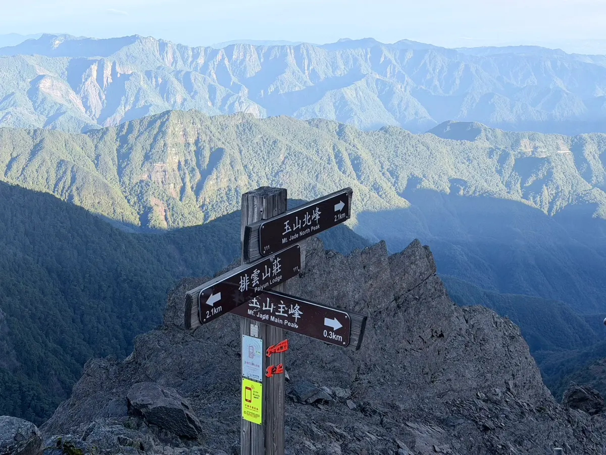 主北岔路的指標牌,寫著玉山北峰 2.1 公里、玉山主峰 0.3 公里、排雲山莊 2.1 公里,背景是清晨的層疊山脈