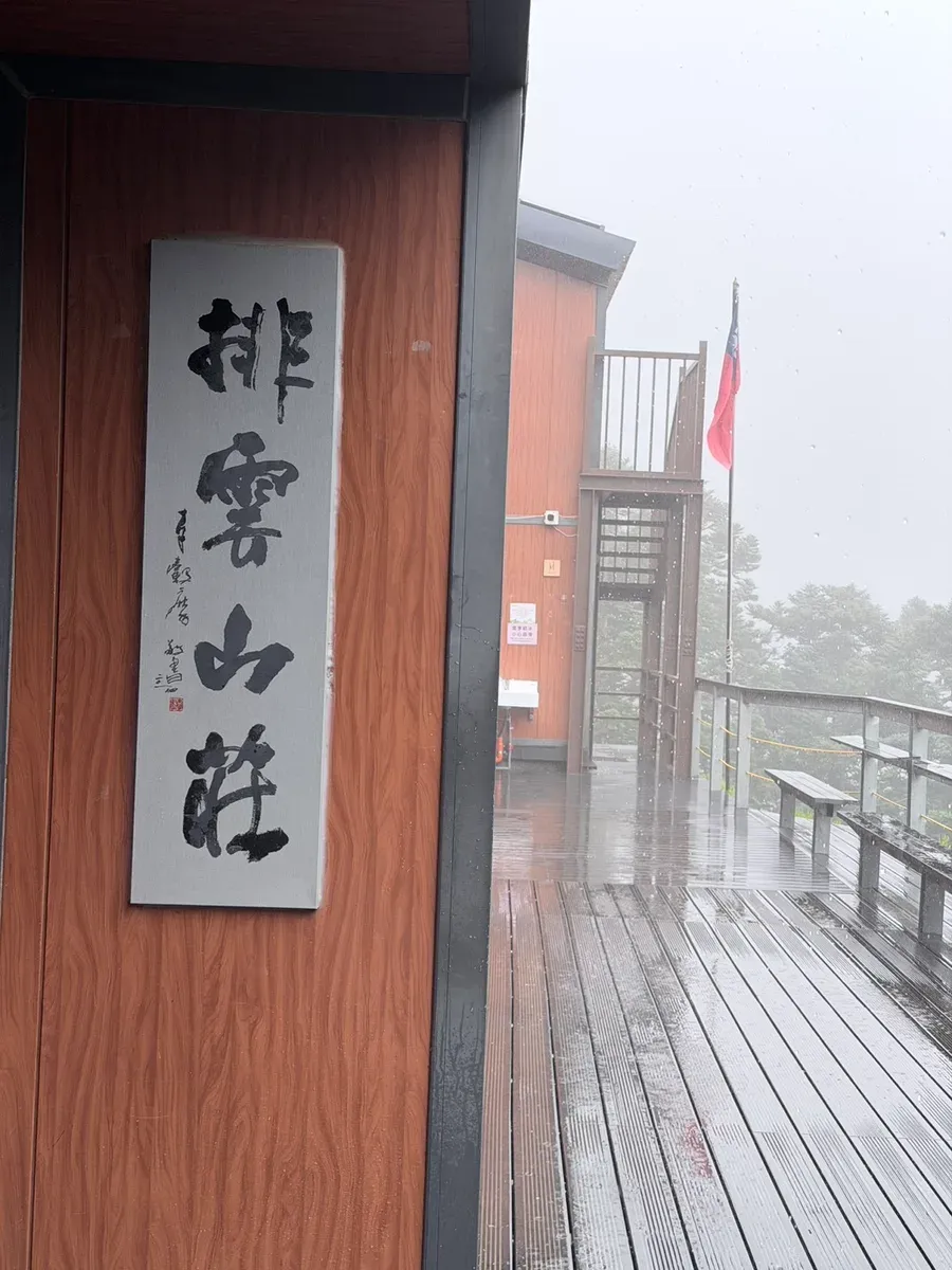 大雨中的排雲山莊,門口掛著書法「排雲山莊」匾額,木棧道全濕、雨滴清晰可見
