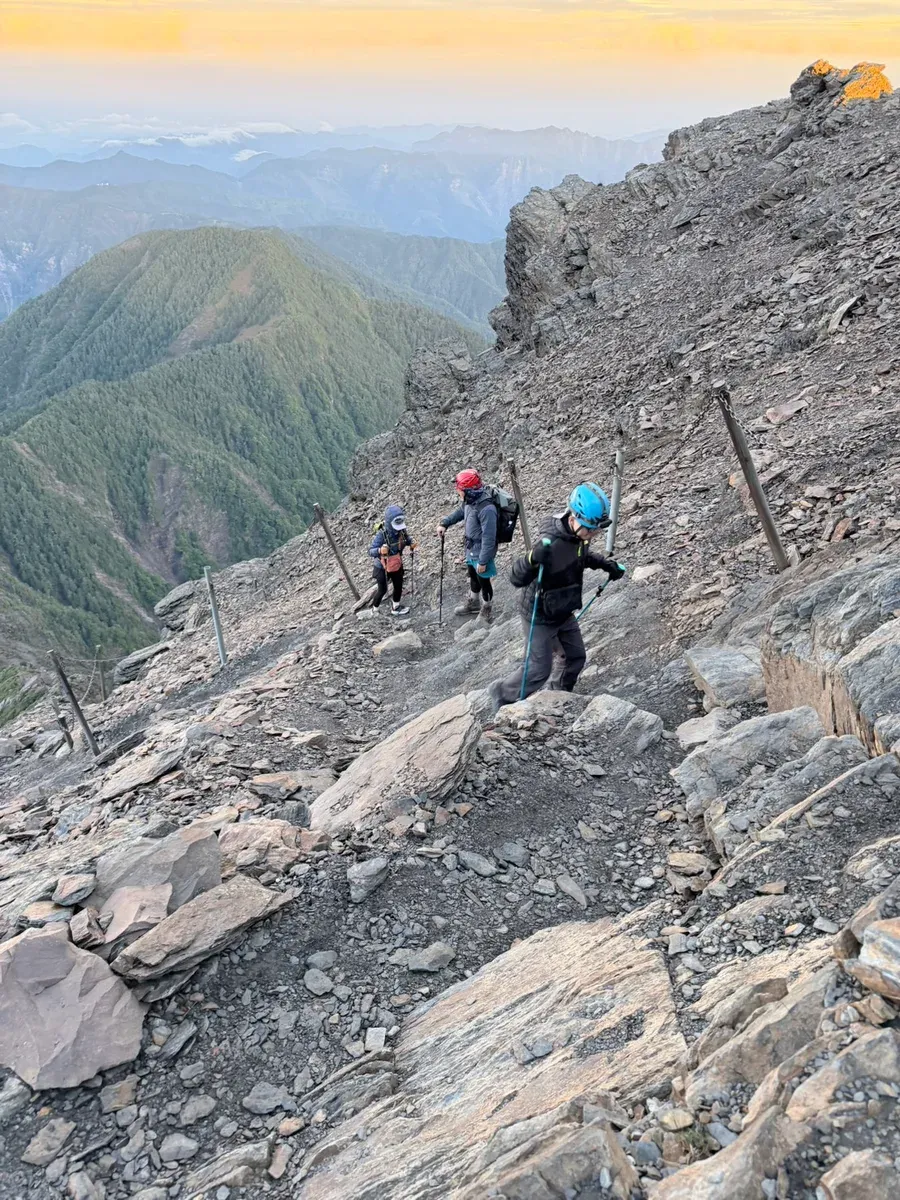 天亮後的玉山碎石坡路段,山友沿著架設鐵樁與鏈條的碎石路徑上行,多數人戴著岩盔
