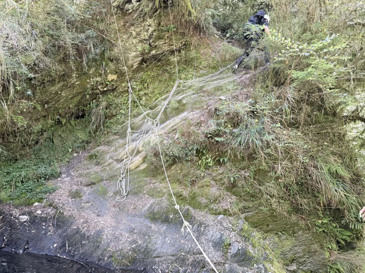 820 林道 8.4K 瀑布旁的濕滑岩壁，架著繩子讓登山者抓著通過