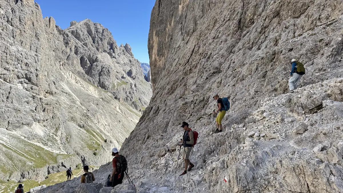 下山路段沿著陡峭的灰色岩壁邊緣，健行者拿著登山杖往下走，岩石上有紅白噴漆標記