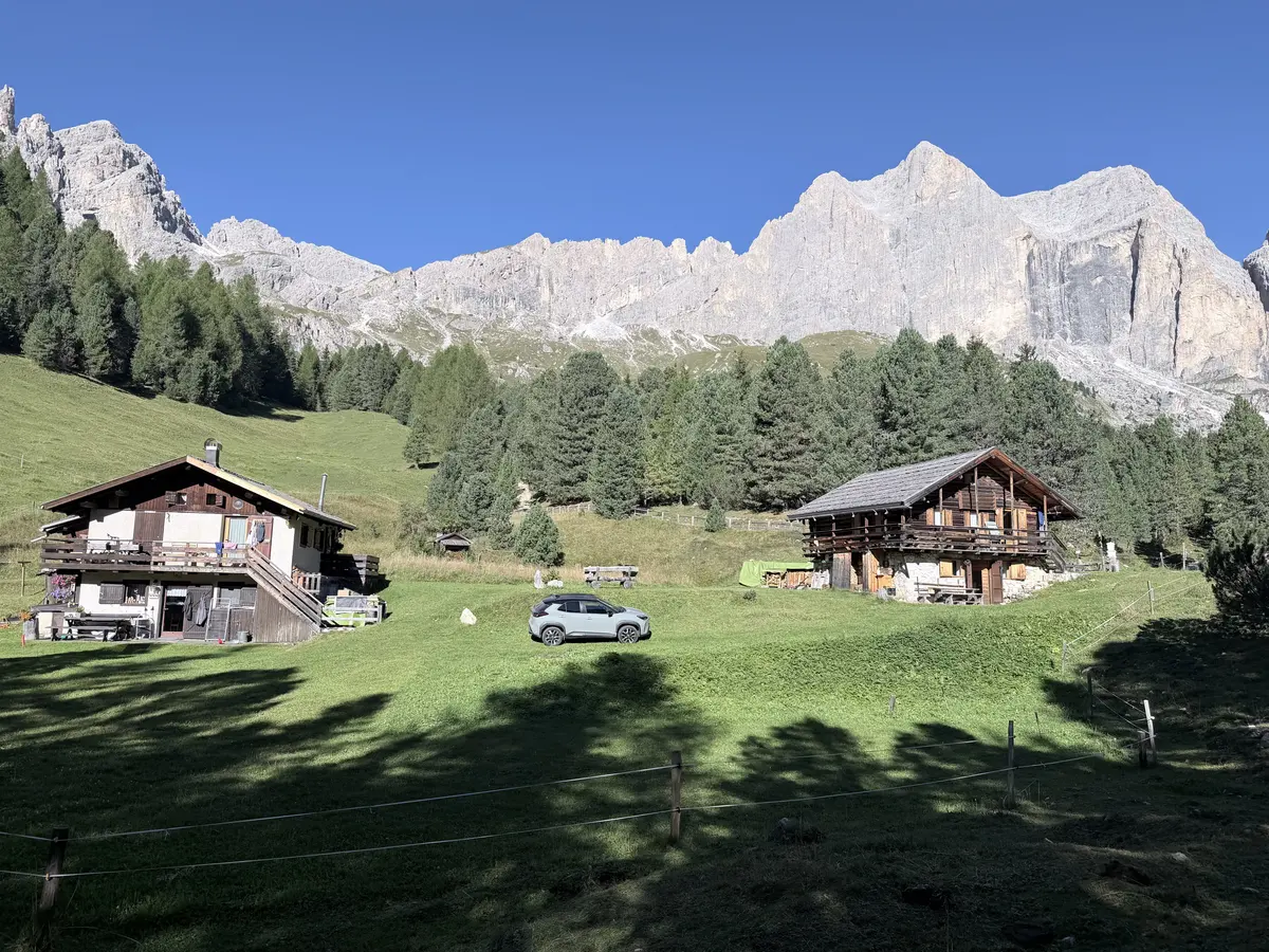 往 Gardeccia 途中的草地上有兩棟木造小屋，後方是高聳的灰白色 Rosengarten 岩壁