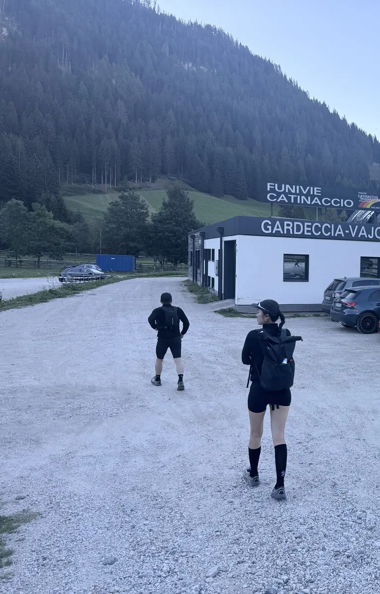 Pera di Fassa 的 Vajolet 纜車站停車場，碎石地面上兩位健行者走向寫著 Gardeccia-Vajolet 的纜車站建築