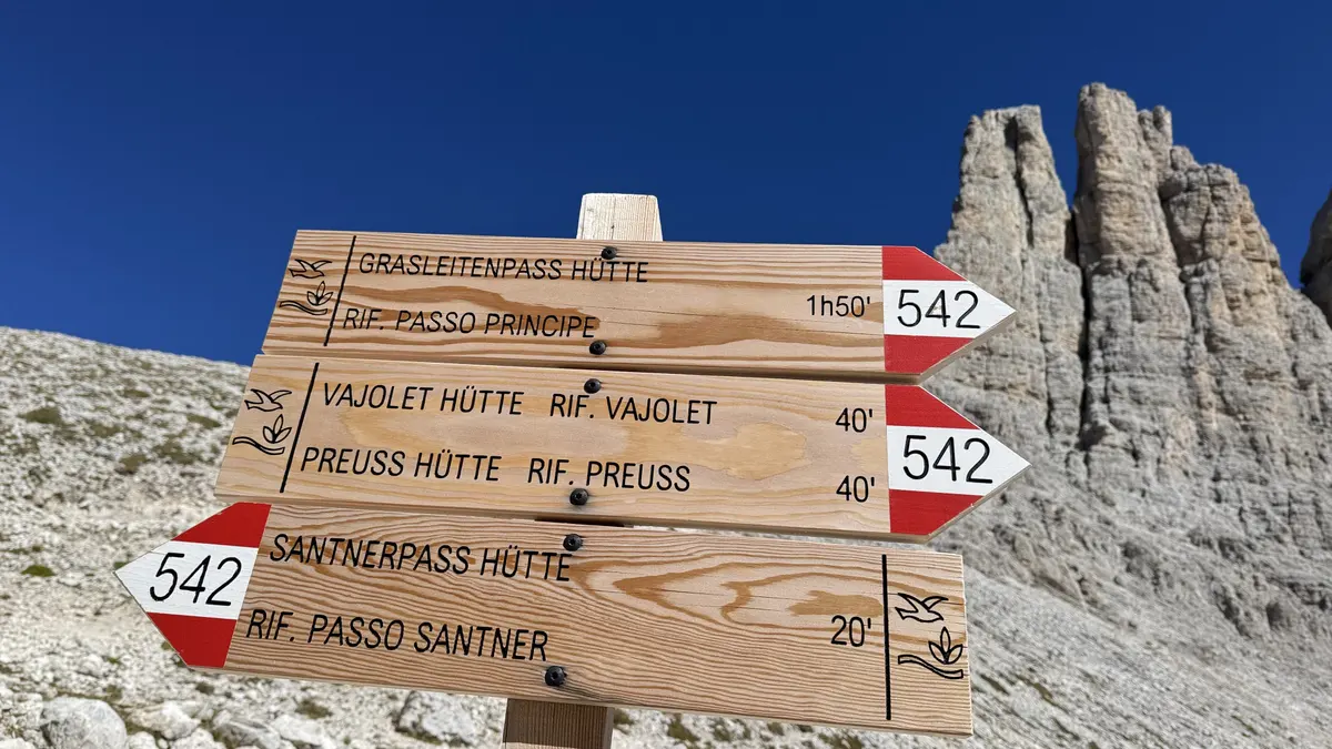 Gartlhütte 旁的木製路牌，標示 542 號步道往 Santnerpass Hütte 20 分鐘、往 Vajolet 與 Preuss 40 分鐘，後方是 Vajolet 三塔