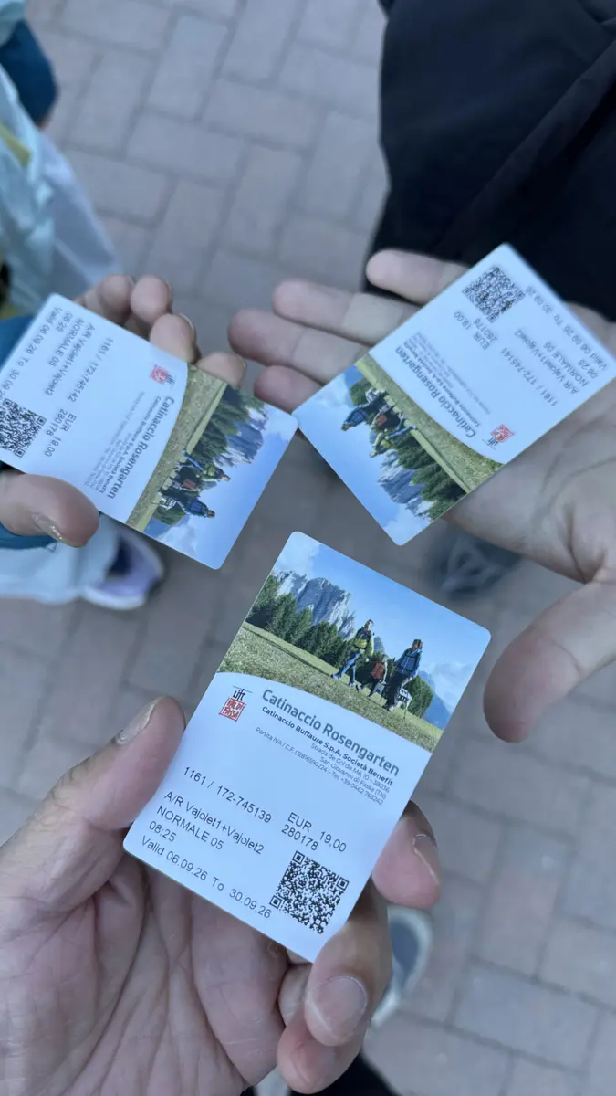 三隻手拿著 Catinaccio Rosengarten 纜車來回票，票面印著 QR Code 與森林照片