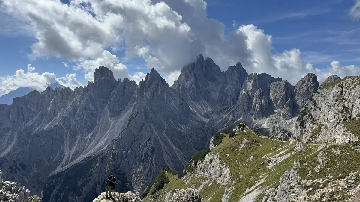 Cadini di Misurina 的鋸齒狀尖峰群，左下角岩石上有人站著拍照，右側是長滿青草的山稜