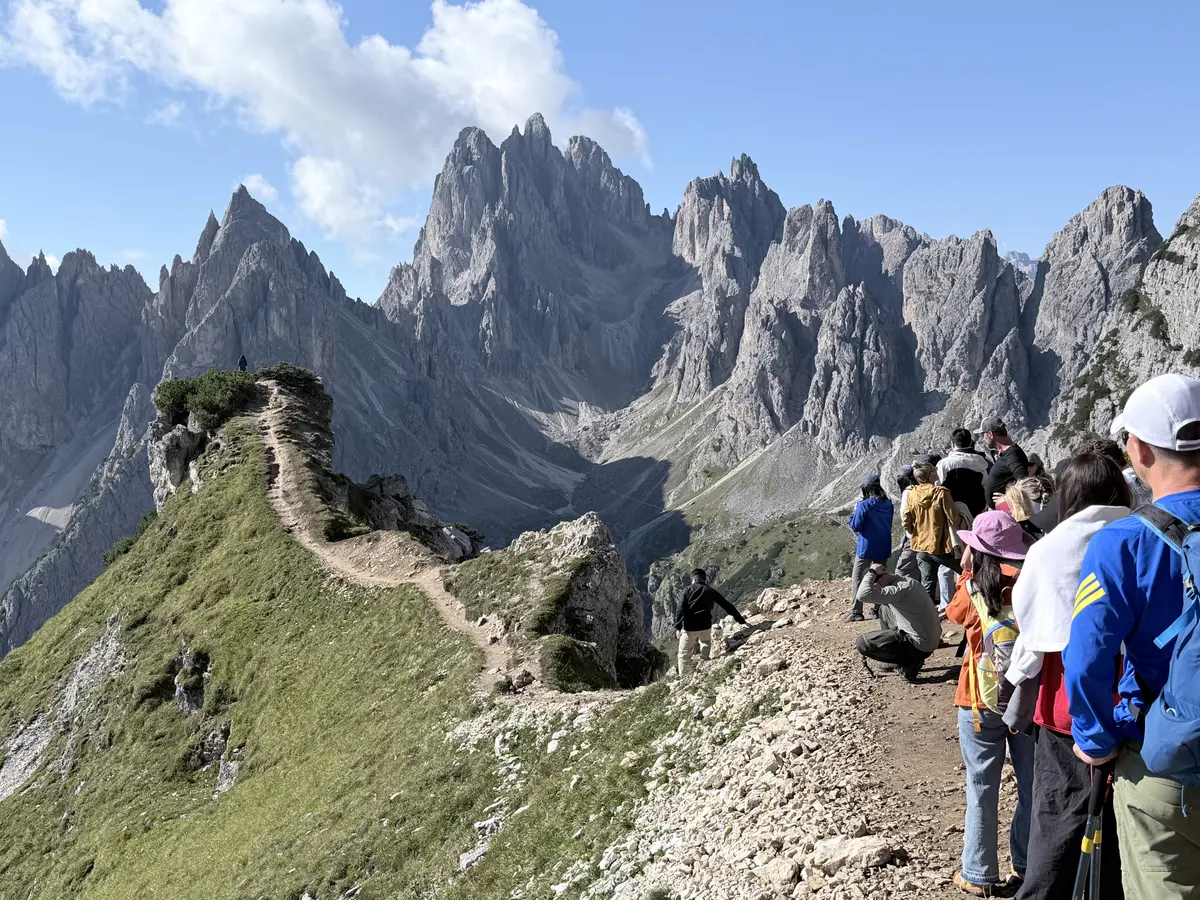 Cadini di Misurina 拍照點前沿著山稜小路排隊的遊客，前方是一整排灰色尖峰群