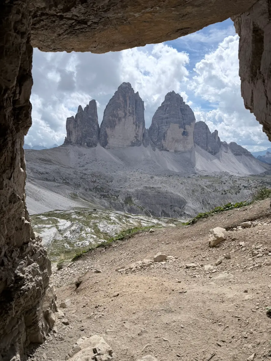 從 Grotta delle Tre Cime 山洞裡往外看，洞口岩壁框住遠方並排的三尖峰