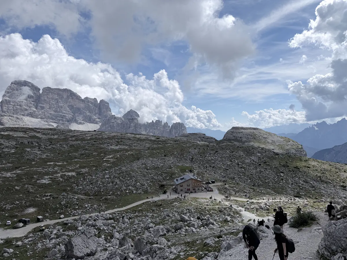 過了 Rifugio Lavaredo 往埡口爬升的寬闊步道，登山客走在碎石路上，下方是 Lavaredo 山屋