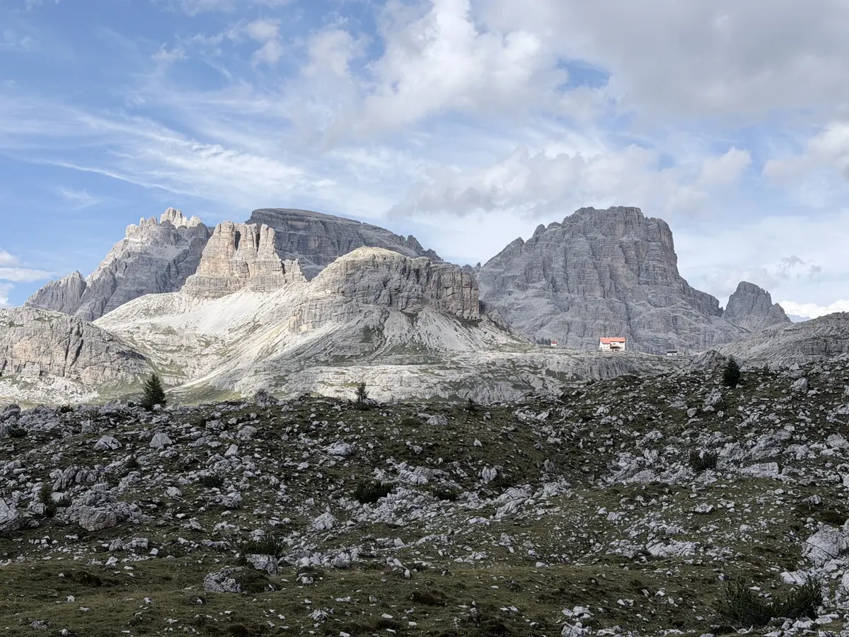 往 Malga Langalm 途中的碎石地形，滿地大小不一的岩塊，遠方岩峰下有一間紅屋頂山屋