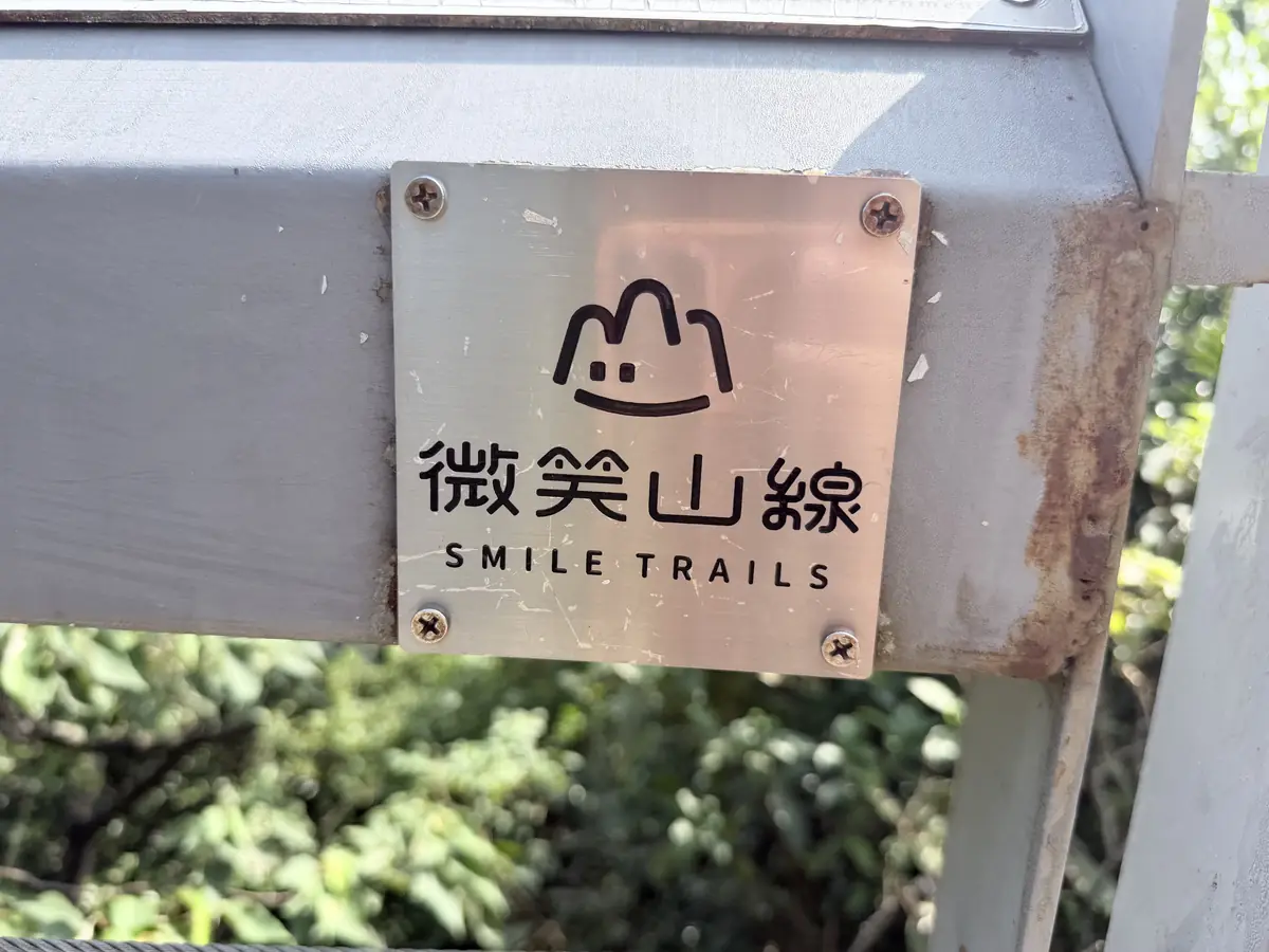 步道欄杆上的微笑山線銅牌，上面有笑臉山形標誌和 SMILE TRAILS 字樣