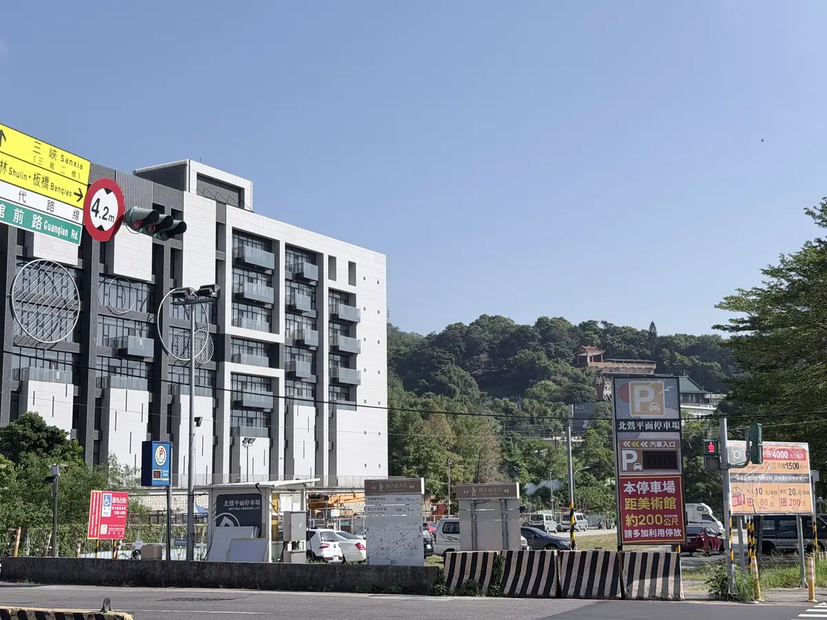 北鶯平面停車場的入口看板，旁邊的費率牌寫著平日每半小時 10 元、假日每半小時 20 元，背後就是鶯歌石所在的山