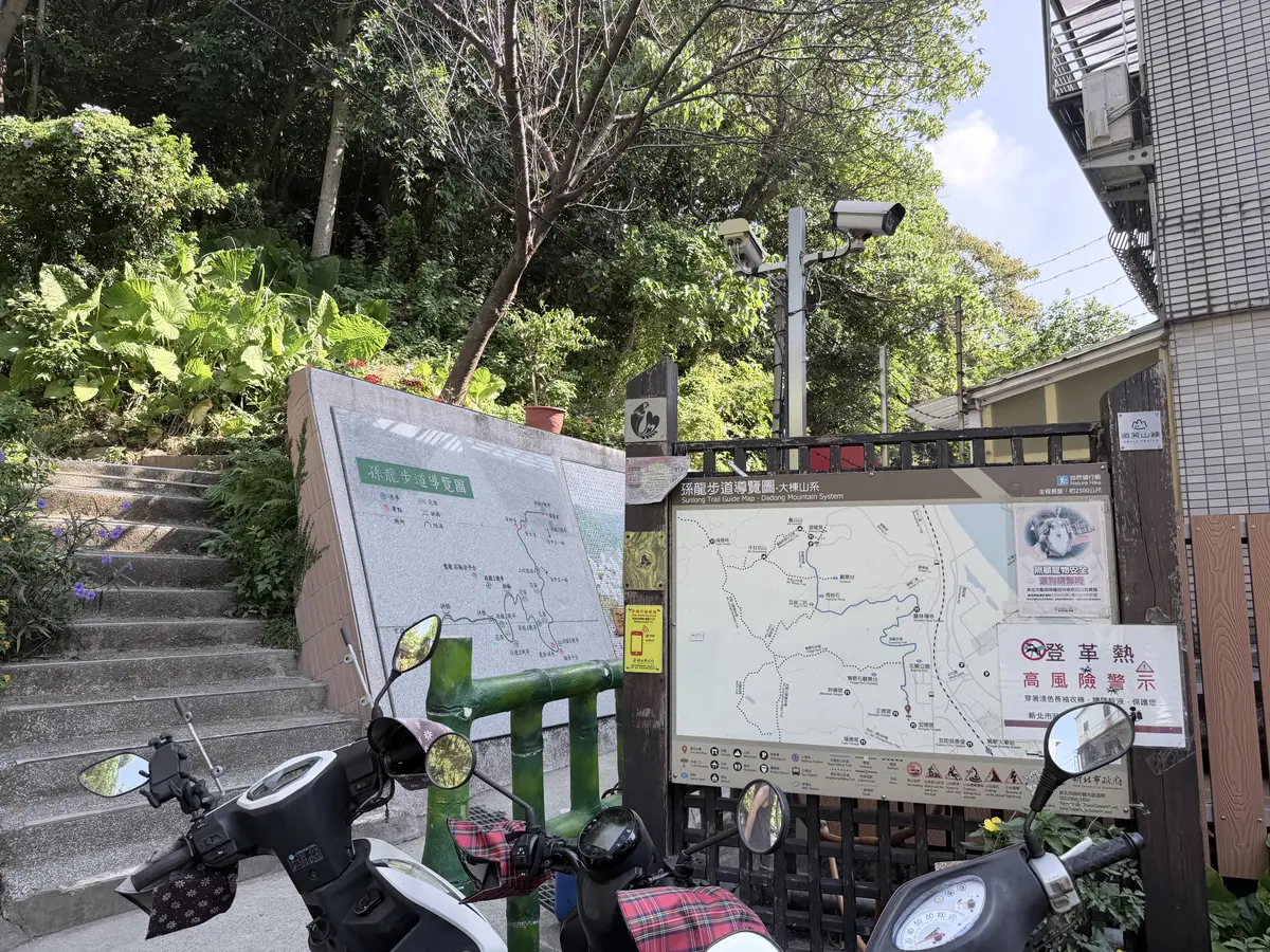 宏德宮旁的孫龍步道登山口，牆上有孫龍步道導覽圖和大棟山系導覽圖，前面停著幾台機車