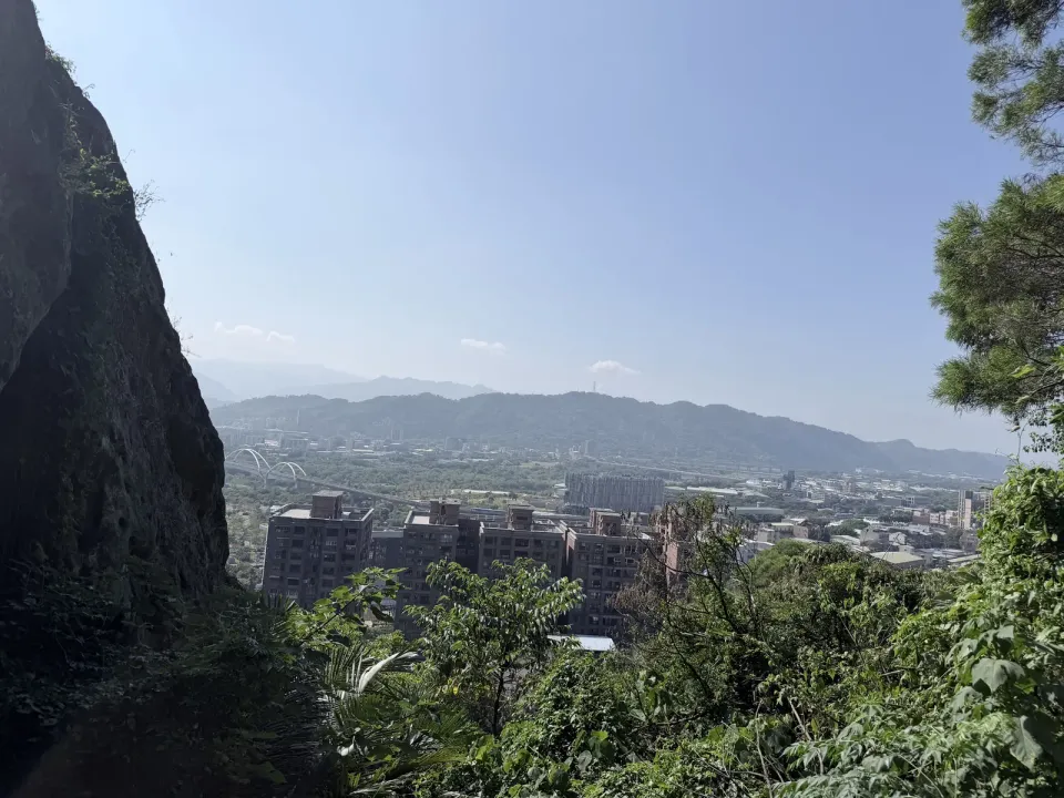 從鶯歌石觀景台往外看，左邊是鶯歌石巨岩的岩壁，下方是鶯歌市區和拱橋，遠處是青色山稜